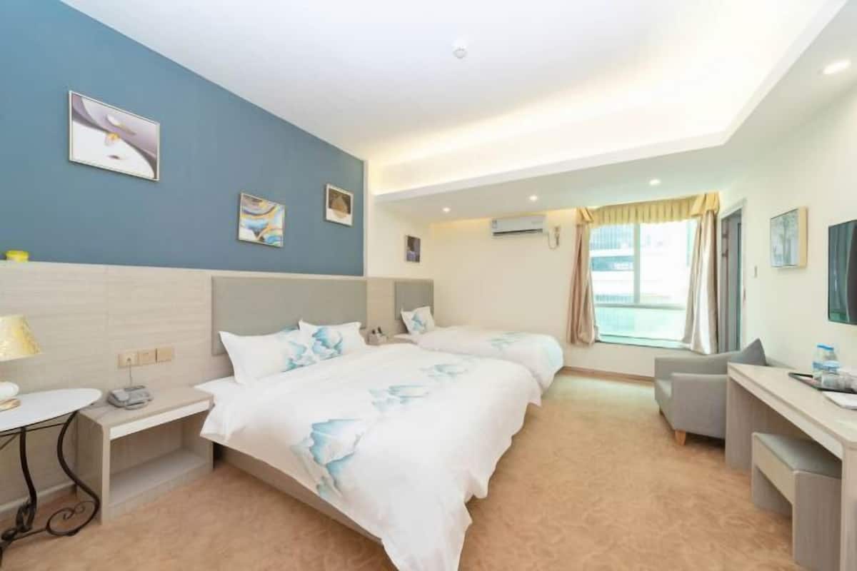 Habitación de hotel con dos camas, un escritorio, una silla y una ventana con cortinas.