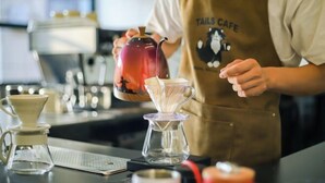 Une personne, vêtue d'un tablier de café, verse du café dans une carafe en verre.