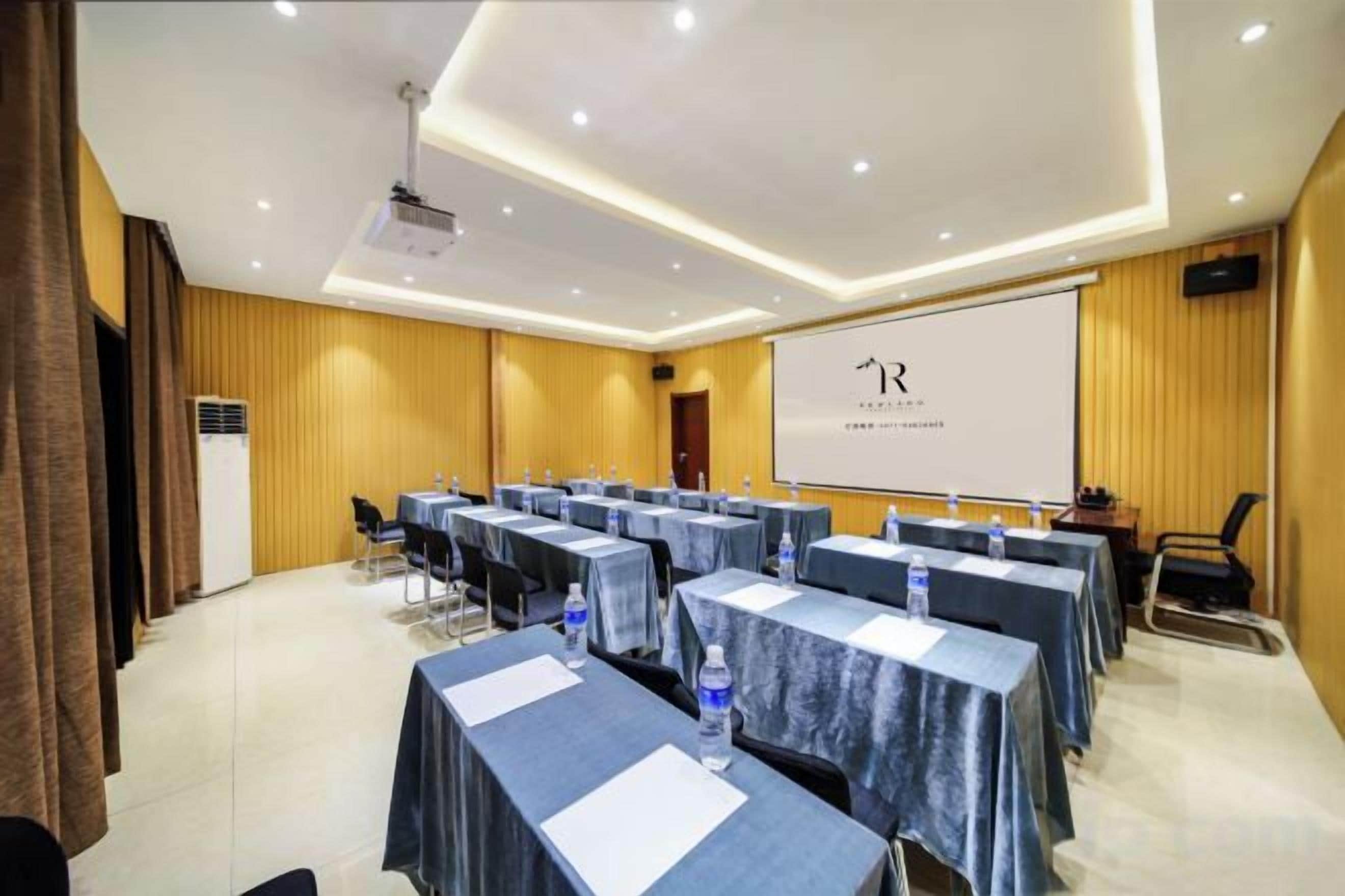 A conference room with tables, chairs, a projector, and a presentation screen.