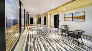 Un hall d’entrée spacieux, doté d’un sol à motifs, de tableaux encadrés aux murs et d’un coin salon avec des chaises et une table.
