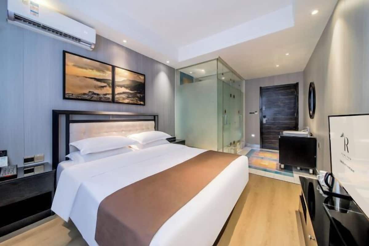 Ein modernes Hotelzimmer mit einem großen Bett, einer Duschkabine aus Glas und einem Flachbildfernseher.