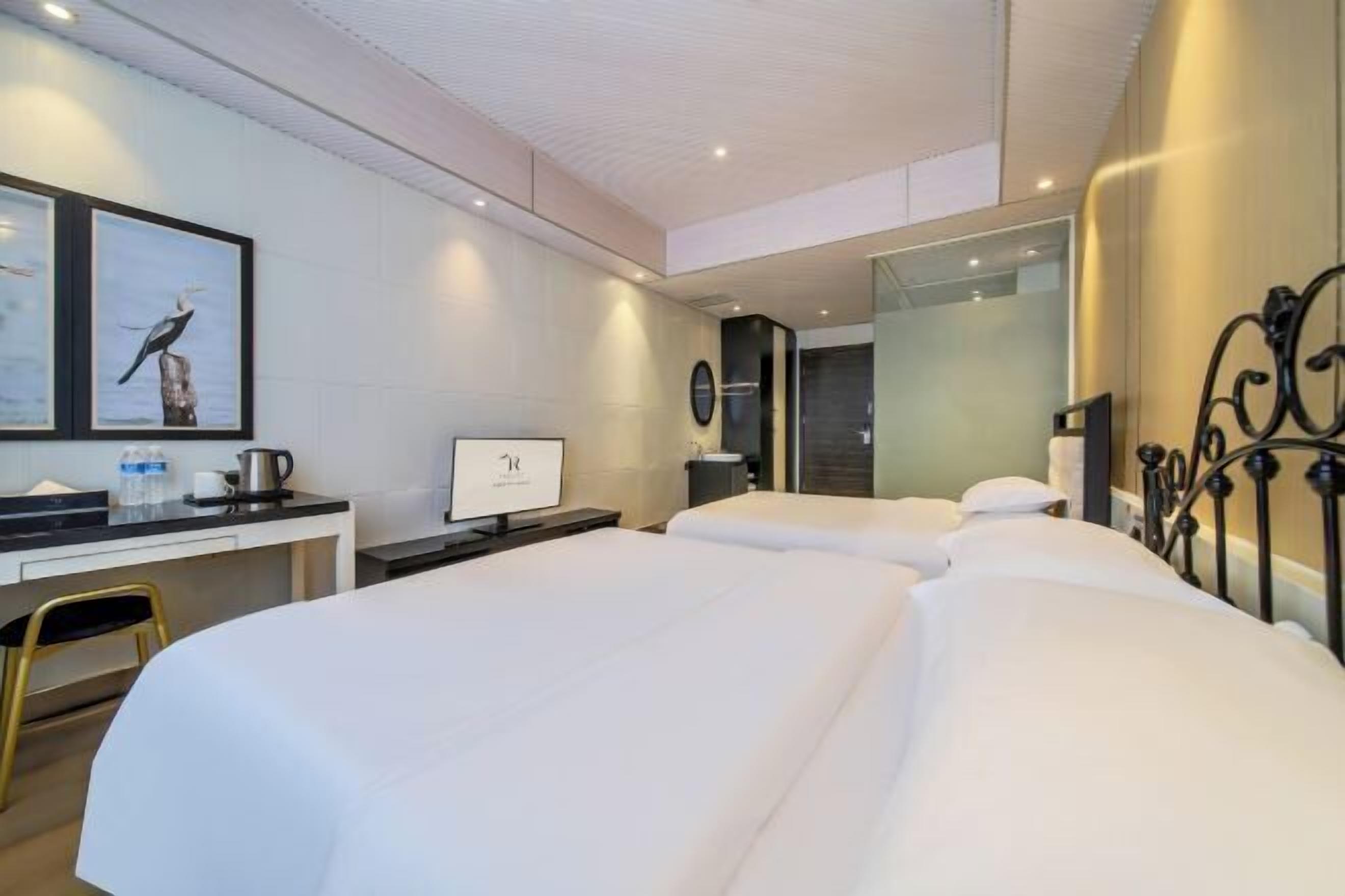 A modern hotel room with two beds, a desk with a computer, and framed artwork on the wall.