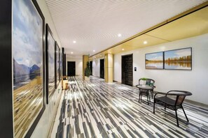 A hotel corridor with a patterned floor, framed artwork on the walls, and seating areas.