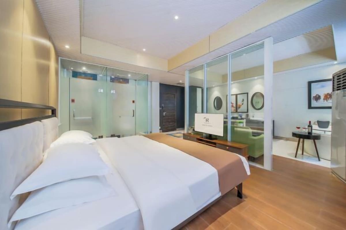 Ein modernes Hotelzimmer mit einem großen Bett, einem Schreibtisch und einer Glastrennwand, die den Raum vom Flur abteilt.