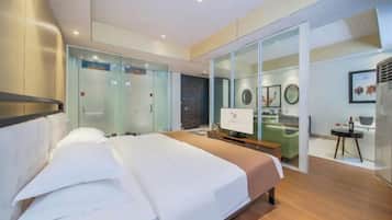 Quarto de hotel moderno com uma cama grande, uma escrivaninha e um separador de vidro que divide o quarto do corredor.