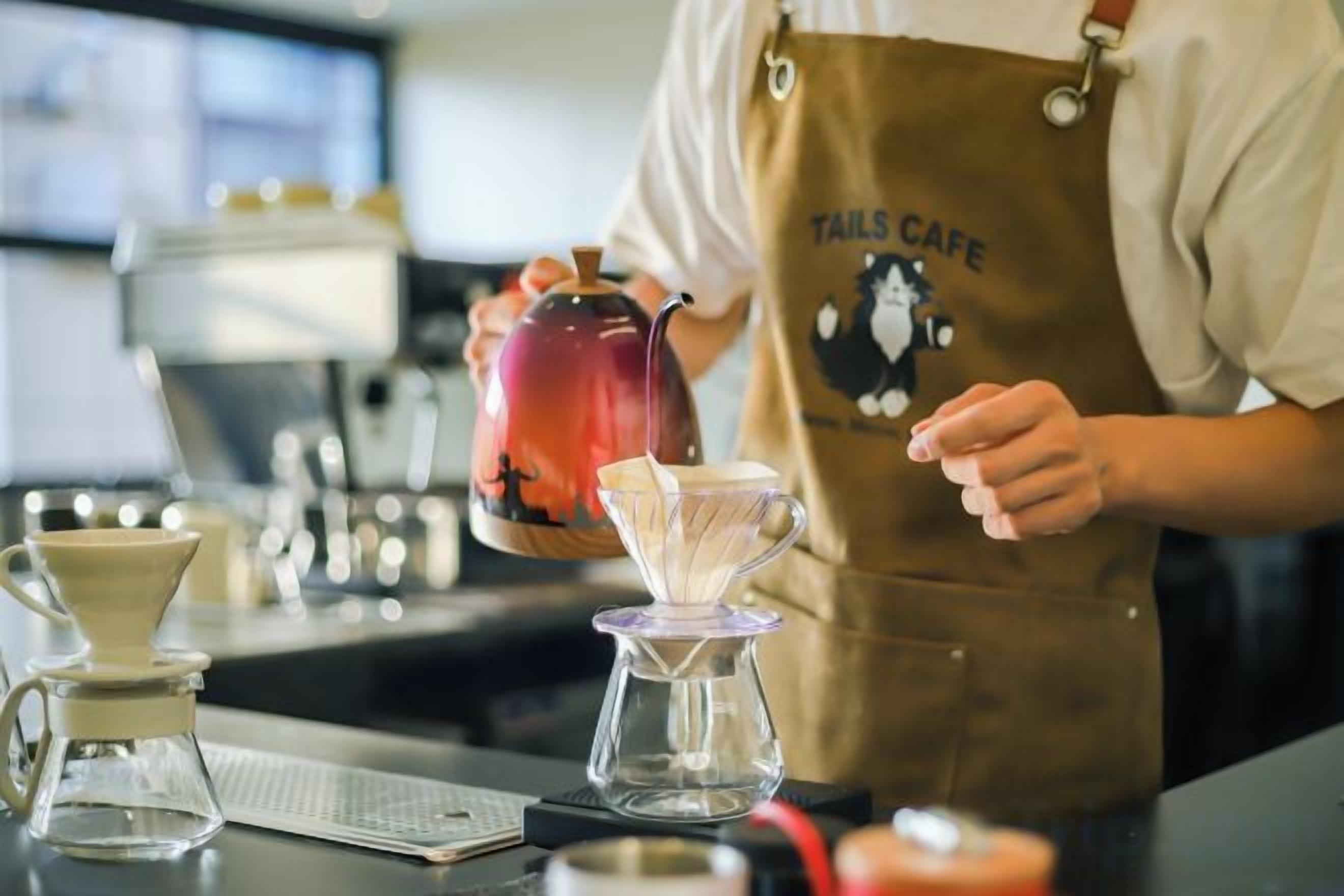 A person in a cafe apron pouring a drink into a glass.