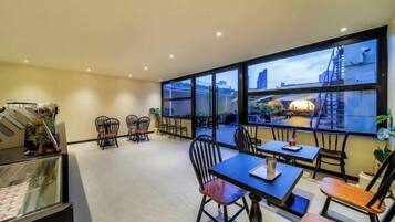 Une chambre d’hôtel dotée d’une grande fenêtre, d’un balcon et d’un coin repas avec chaises et tables.