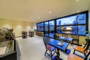 Une chambre d’hôtel dotée d’une grande fenêtre, d’un balcon et d’un coin repas avec chaises et tables.
