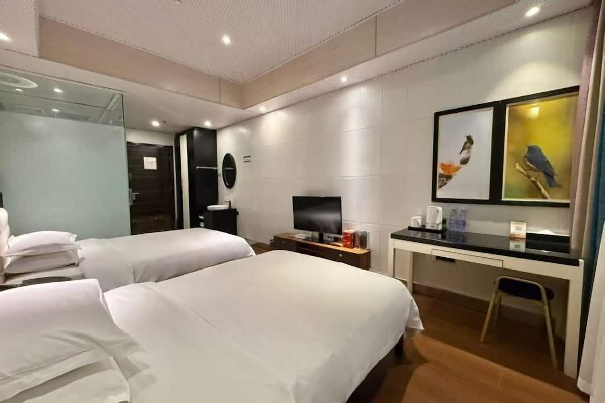 Ein Hotelzimmer mit zwei Betten, einem Schreibtisch, einem Fernseher und Bildern an der Wand.