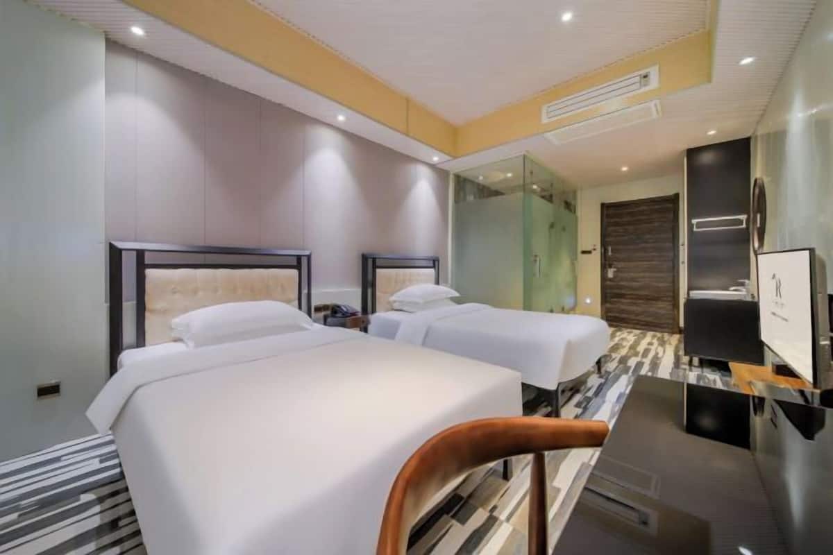 Ein Hotelzimmer mit zwei Betten, einem Schreibtisch, einem Stuhl, einem Spiegel und einer Dusche.