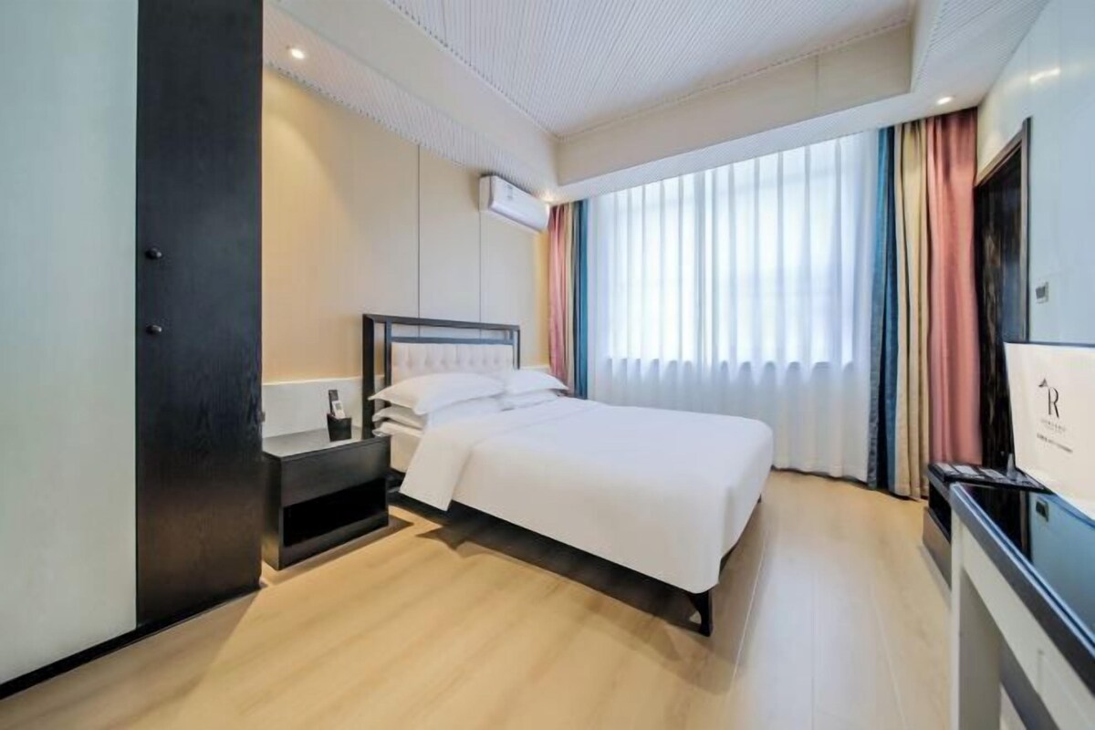 Ein modernes Hotelzimmer mit einem großen Bett, einem Nachttisch, einem Fernseher und einem Kleiderschrank.