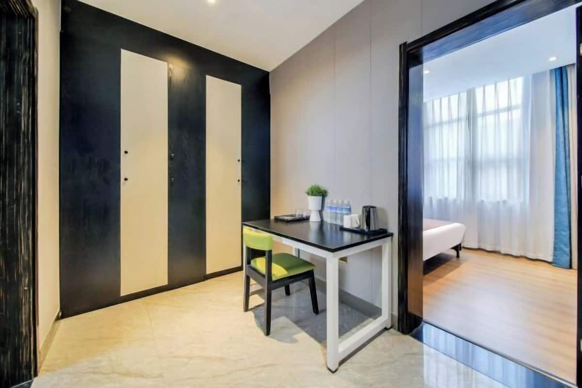 Une chambre moderne équipée d’un bureau, d’une chaise et d’un lit. On y trouve une porte à cadre noir et une fenêtre avec des rideaux.