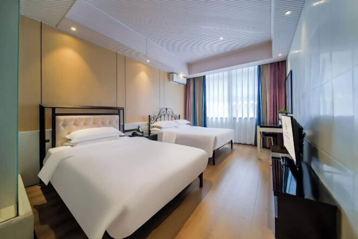 Ein Hotelzimmer mit zwei Betten, einem Fernseher und einem großen Fenster mit Vorhängen.