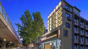 Un hôtel à plusieurs étages, avec un restaurant visible au rez-de-chaussée, une architecture moderne et un arbre devant l’entrée.