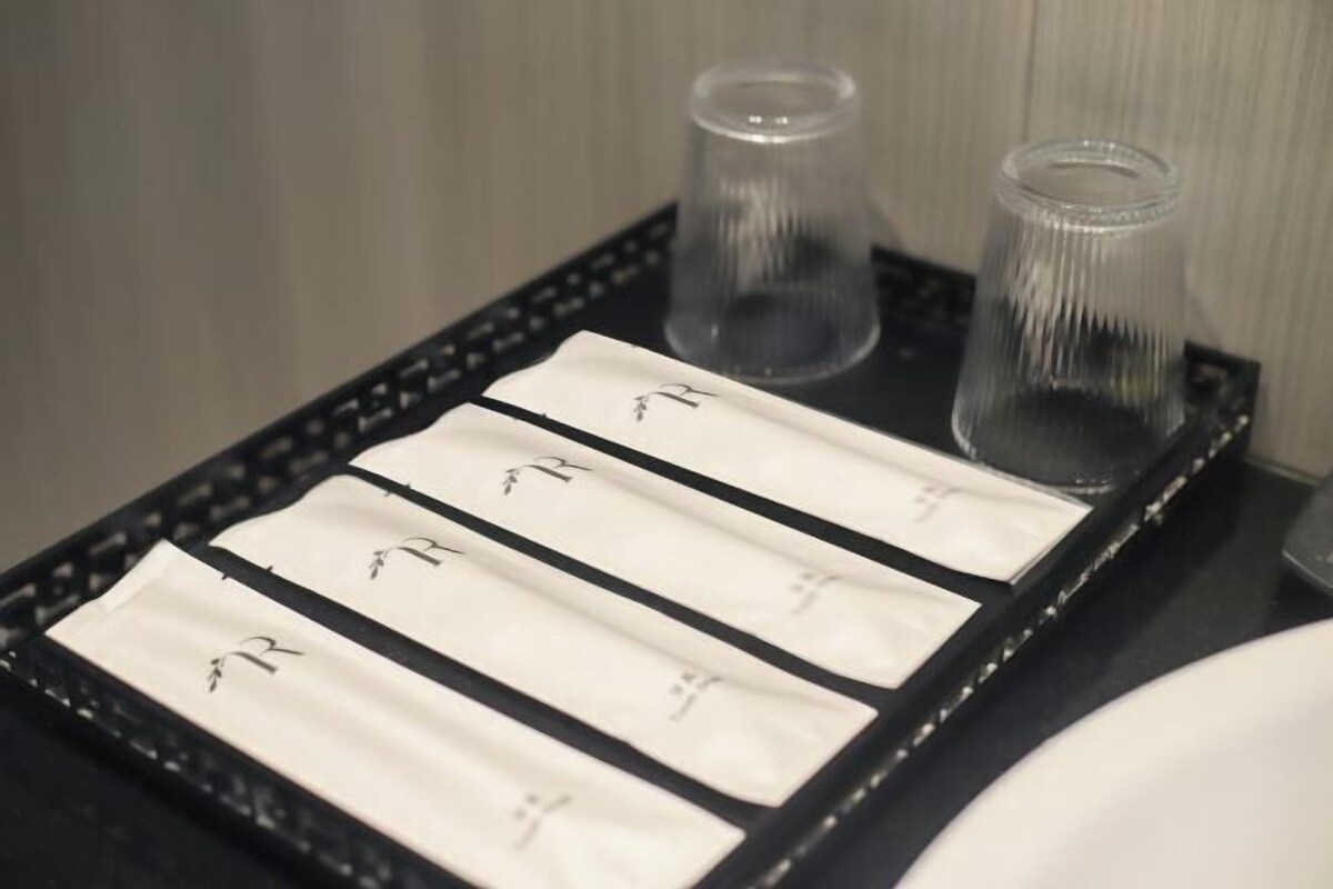 Ein Tablett mit vier weißen Servietten, jede mit einem schwarzen Logo, und zwei klaren Gläsern.