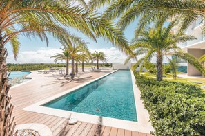 A pool area with wooden decking, lounge chairs, and palm trees.