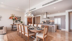 A spacious living area with a dining table set for six, a kitchen with modern appliances, and a large chandelier. - Brand new Aparment w 3BR in Cap Cana (Punta Cana)