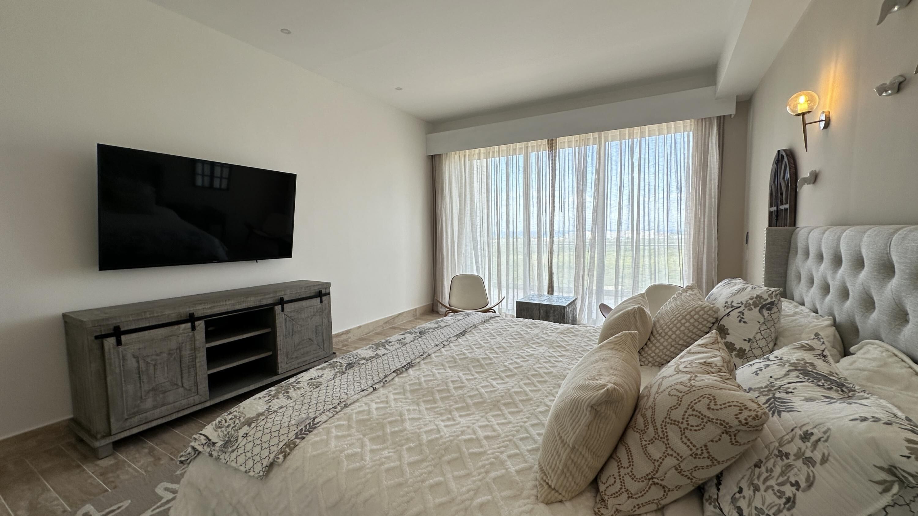 Una camera da letto moderna con un letto grande, una TV a parete e vista sull'esterno attraverso ampie finestre.