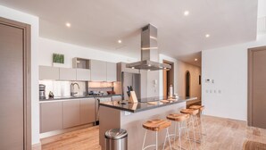 A modern kitchen with a central island, bar stools, and stainless steel appliances. - Brand new Aparment w 3BR in Cap Cana (Punta Cana)