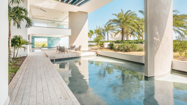 A modern outdoor pool area with a wooden deck, lounge chairs, and palm trees. - Brand new Aparment w 3BR in Cap Cana (Punta Cana)