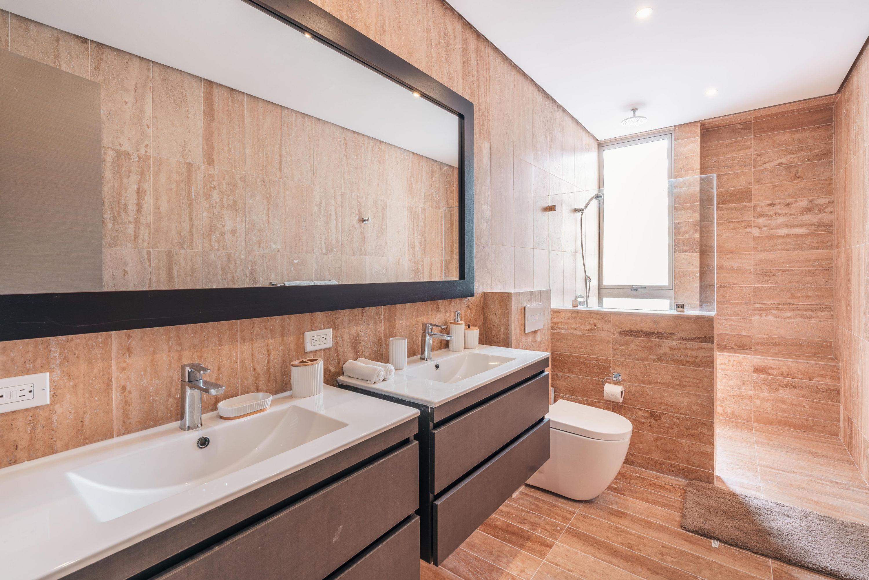A modern bathroom with two sinks, a large mirror, and a shower area.
