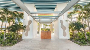 A modern hotel lobby with a central reception desk, surrounded by palm trees and a tiled floor. - Brand new Aparment w 3BR in Cap Cana (Punta Cana)