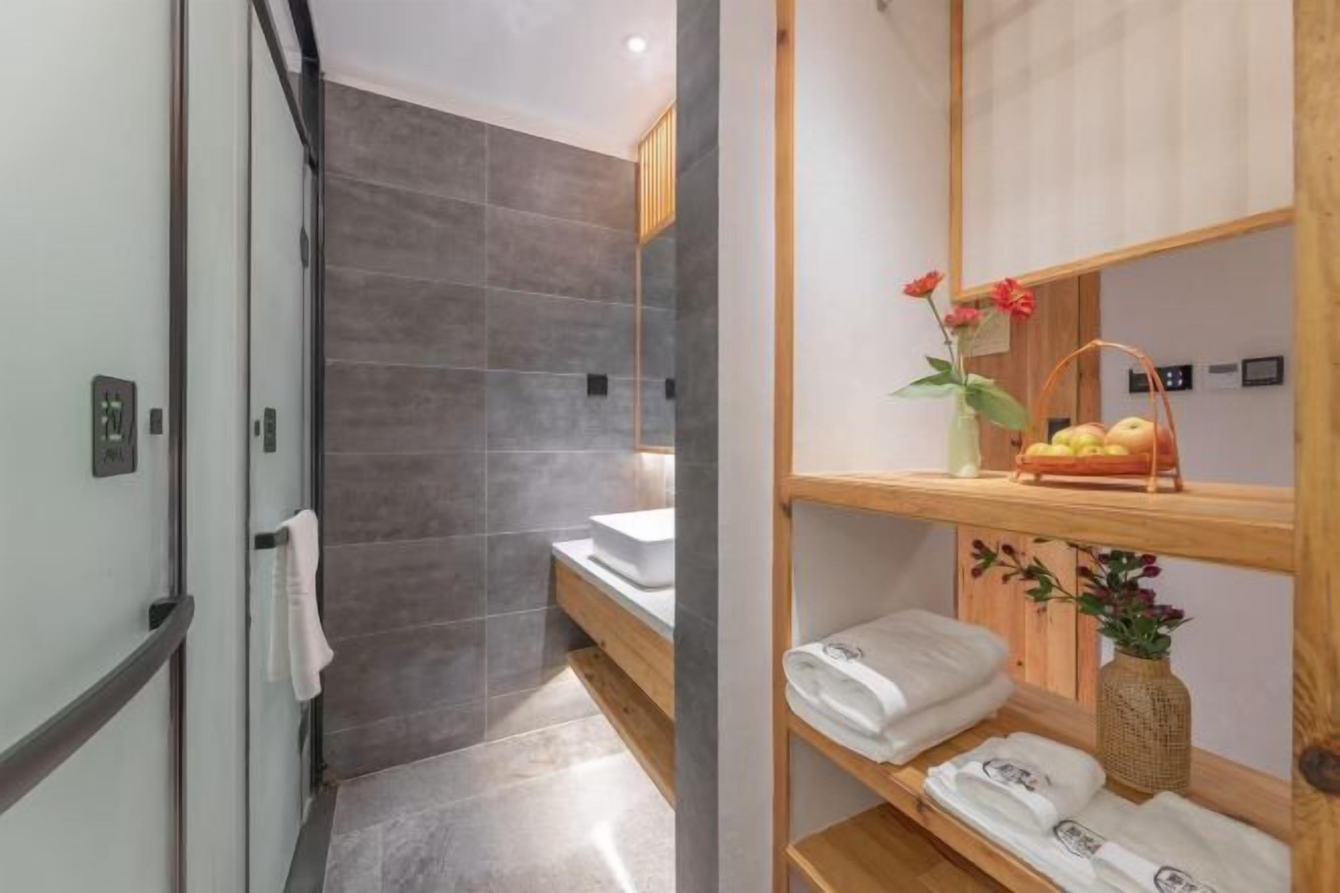Un baño moderno con ducha, lavamanos y un estante de madera con toallas y flores.