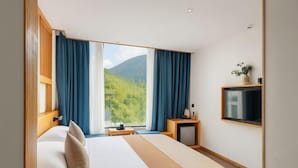 Una habitación de hotel con una cama, televisión, una mesita y una ventana con cortinas.