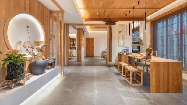 Un interior moderno con techo de madera, un área de comedor central con una mesa larga y un ventanal grande a la derecha.