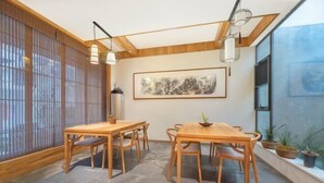 Un comedor con mesas y sillas de madera, un ventanal con vistas, y un cuadro abstracto enmarcado en la pared.