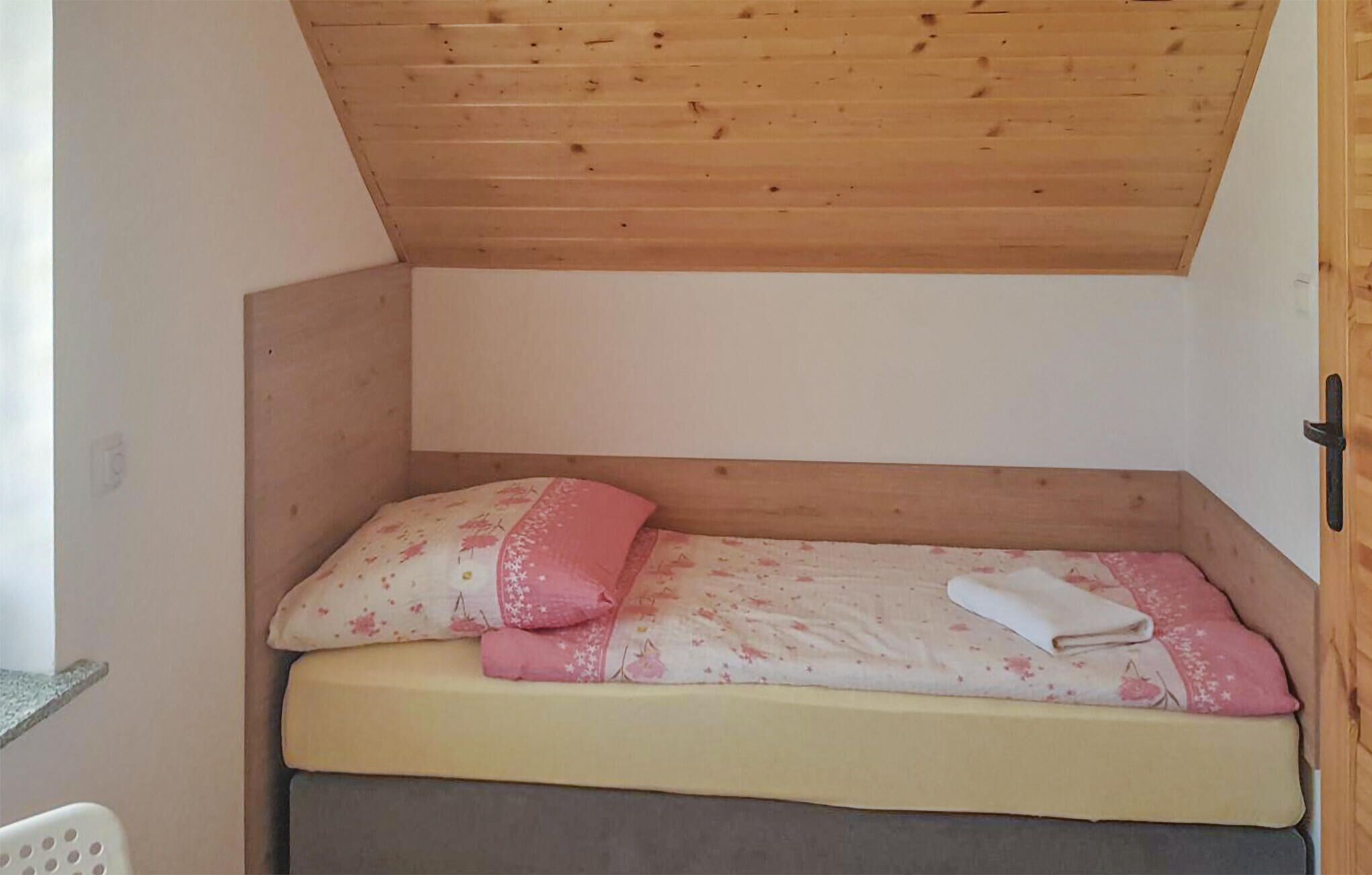 Piccola stanza con struttura in legno, un letto singolo, un cuscino e un asciugamano piegato.