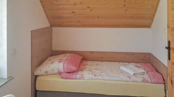 Piccola stanza con struttura in legno, un letto singolo, un cuscino e un asciugamano piegato.
