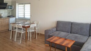 Un espace de vie compact comprenant un coin cuisine, un canapé gris, une table basse en bois et un coin repas avec des chaises blanches.