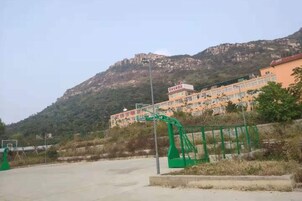 Un edificio con montañas al fondo, una cancha de baloncesto y una valla verde.