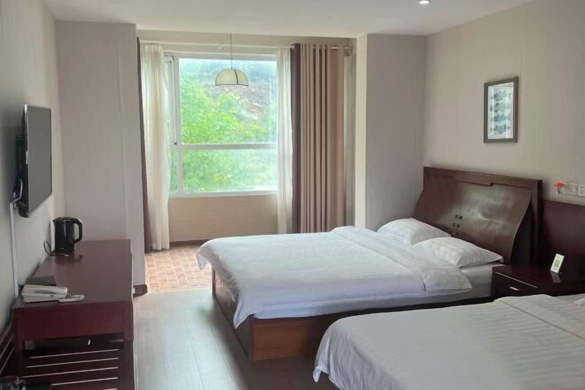 Ein Hotelzimmer mit zwei Betten, einem Fernseher, einer Kaffeemaschine und einem Fenster mit Vorhängen.