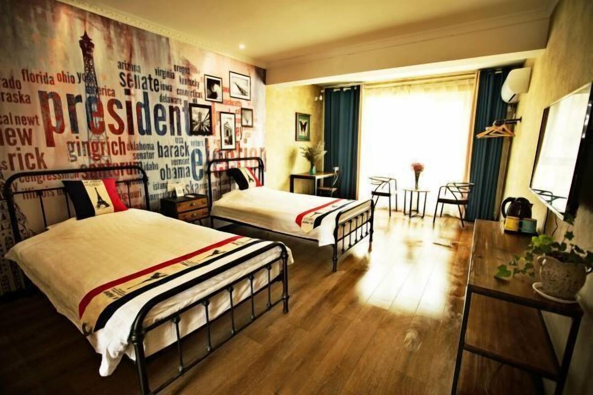 Ein Hotelzimmer mit zwei Betten, einem kleinen Tisch, einem Stuhl, einem Schreibtisch und einem Fenster mit Vorhängen.