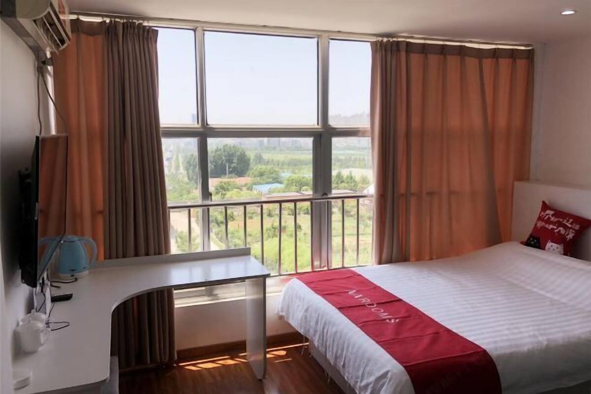 Ein Hotelzimmer mit Bett, Schreibtisch und einem großen Fenster mit Blick auf Grünflächen.