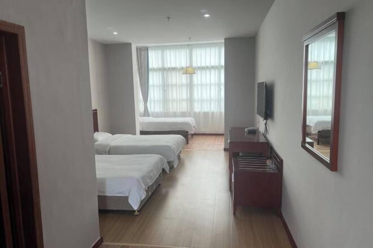 Ein Hotelzimmer mit zwei Betten, einem Schreibtisch, einem Fernseher und einem großen Fenster mit Vorhängen.