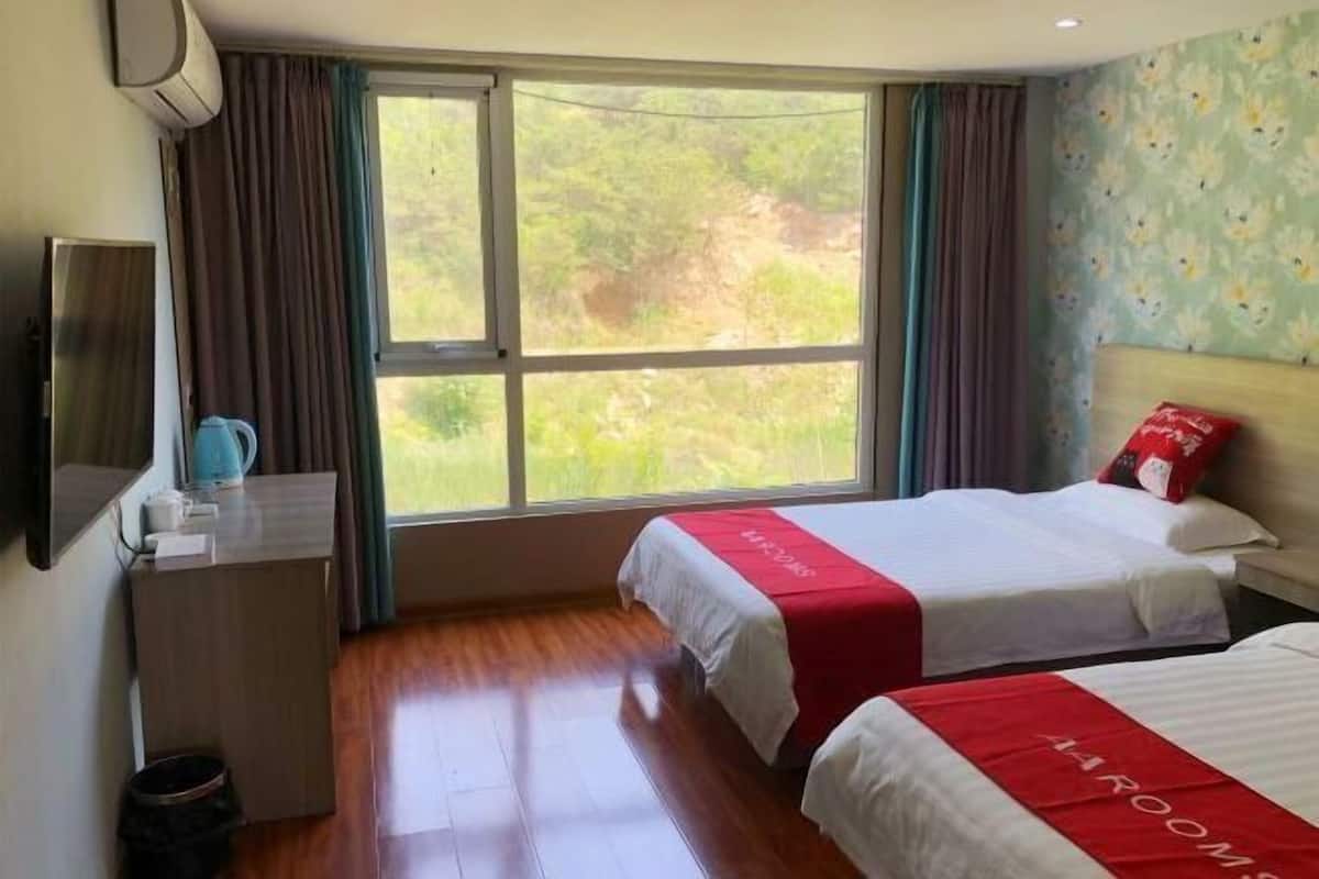 Ein Hotelzimmer mit zwei Betten, einem Schreibtisch, einem Fernseher und einem Fenster mit Blick ins Grüne.