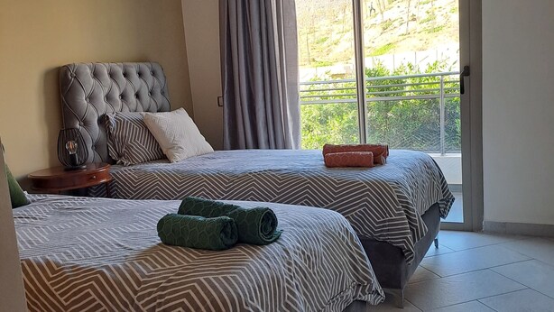 Habitación de hotel con dos camas, un ventanal con vistas a una colina y una puerta corrediza de cristal.
