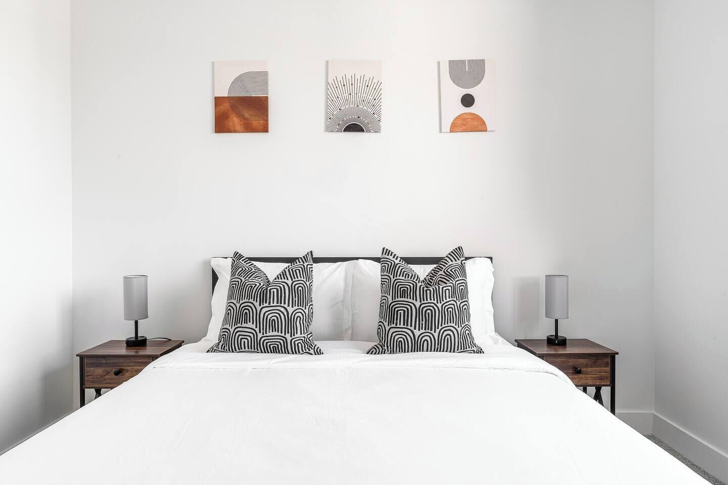 A modern bedroom with a large bed, two bedside tables, and three wall-mounted artworks.