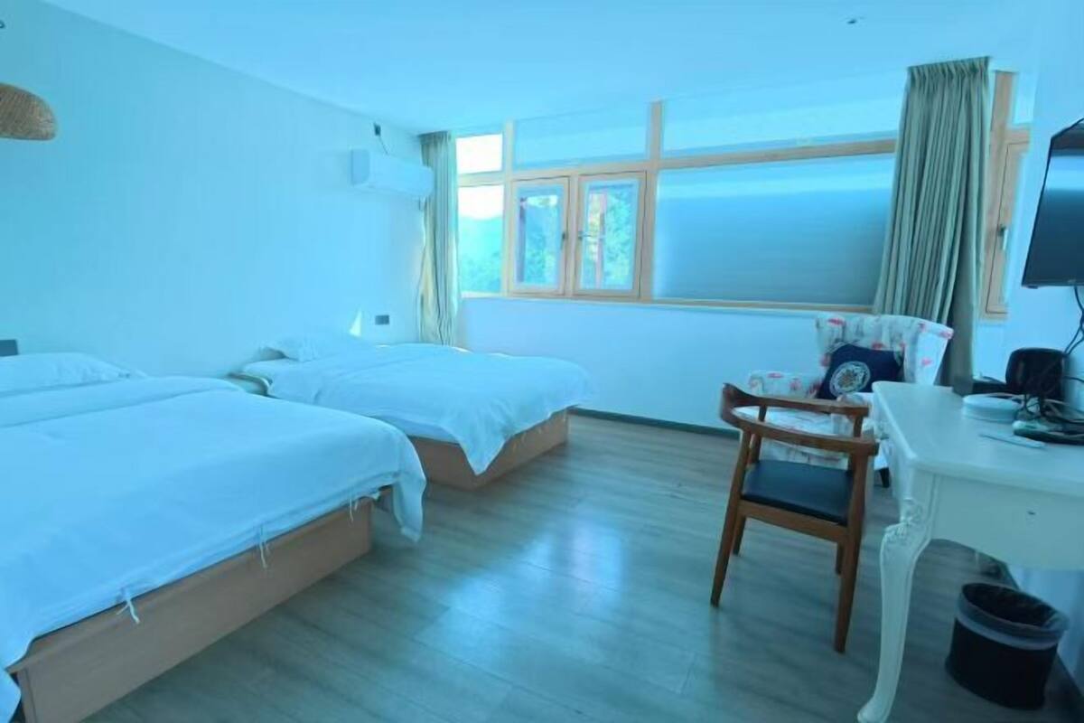 A hotel room with two beds, a desk, a chair, a television, and a window with curtains.