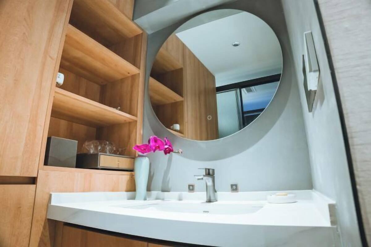 A modern bathroom with a round mirror, wooden shelves, and a white sink.