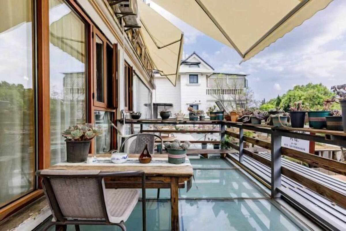 A balcony with a table, chairs, potted plants, and a view of a white building.
