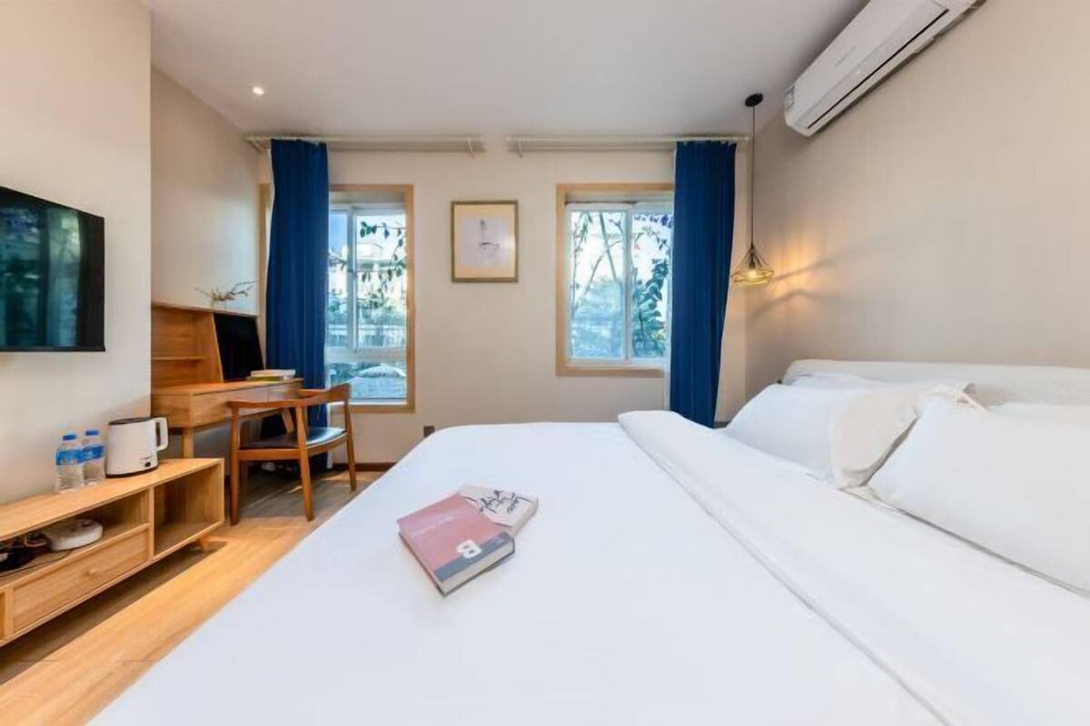 A hotel room with a bed, a desk with a chair, a TV, and a window with curtains.