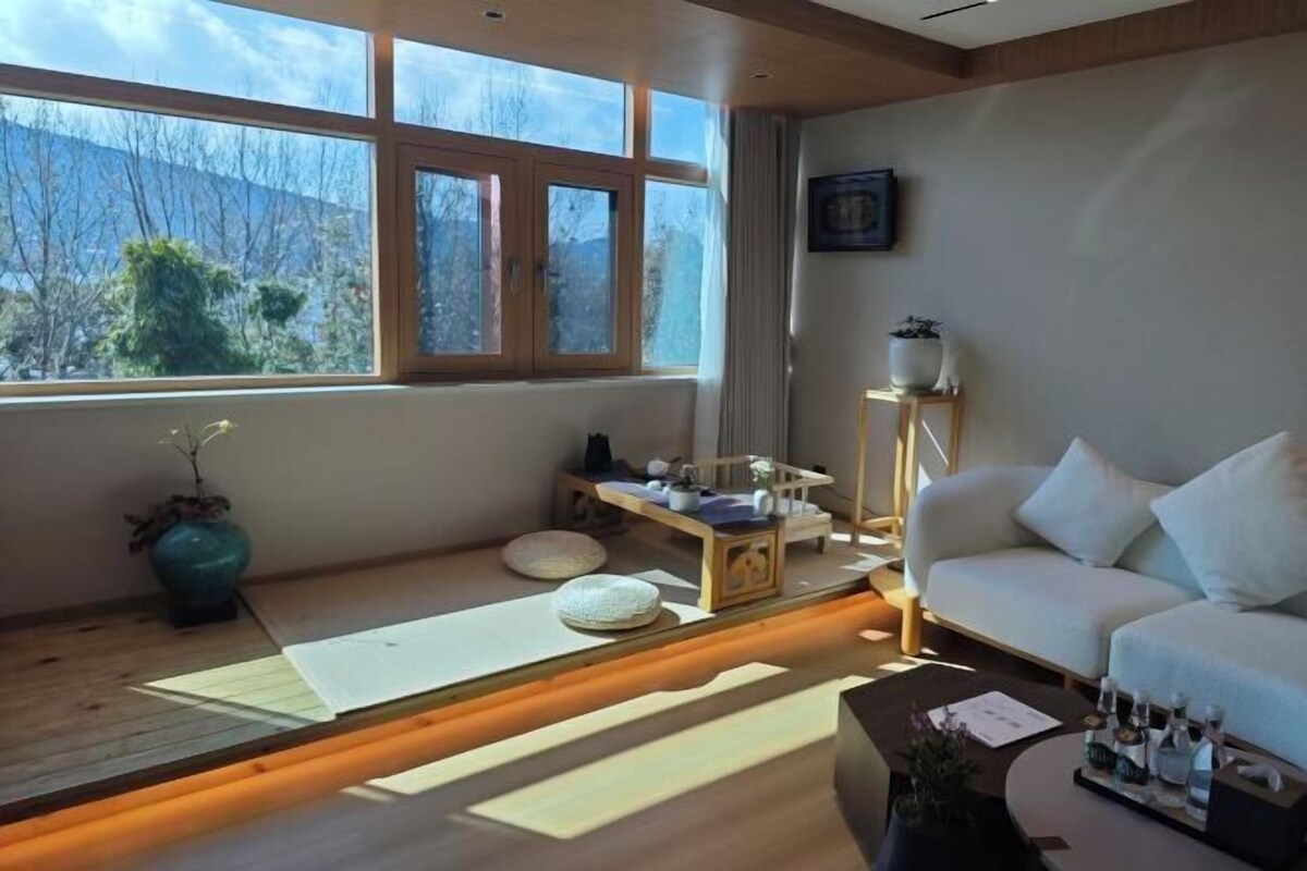 A modern living room with a sofa, a coffee table, and a view of the outdoors through large windows.
