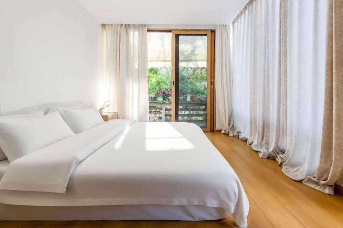 A bedroom with a bed, curtains, and a view of greenery through a sliding door.