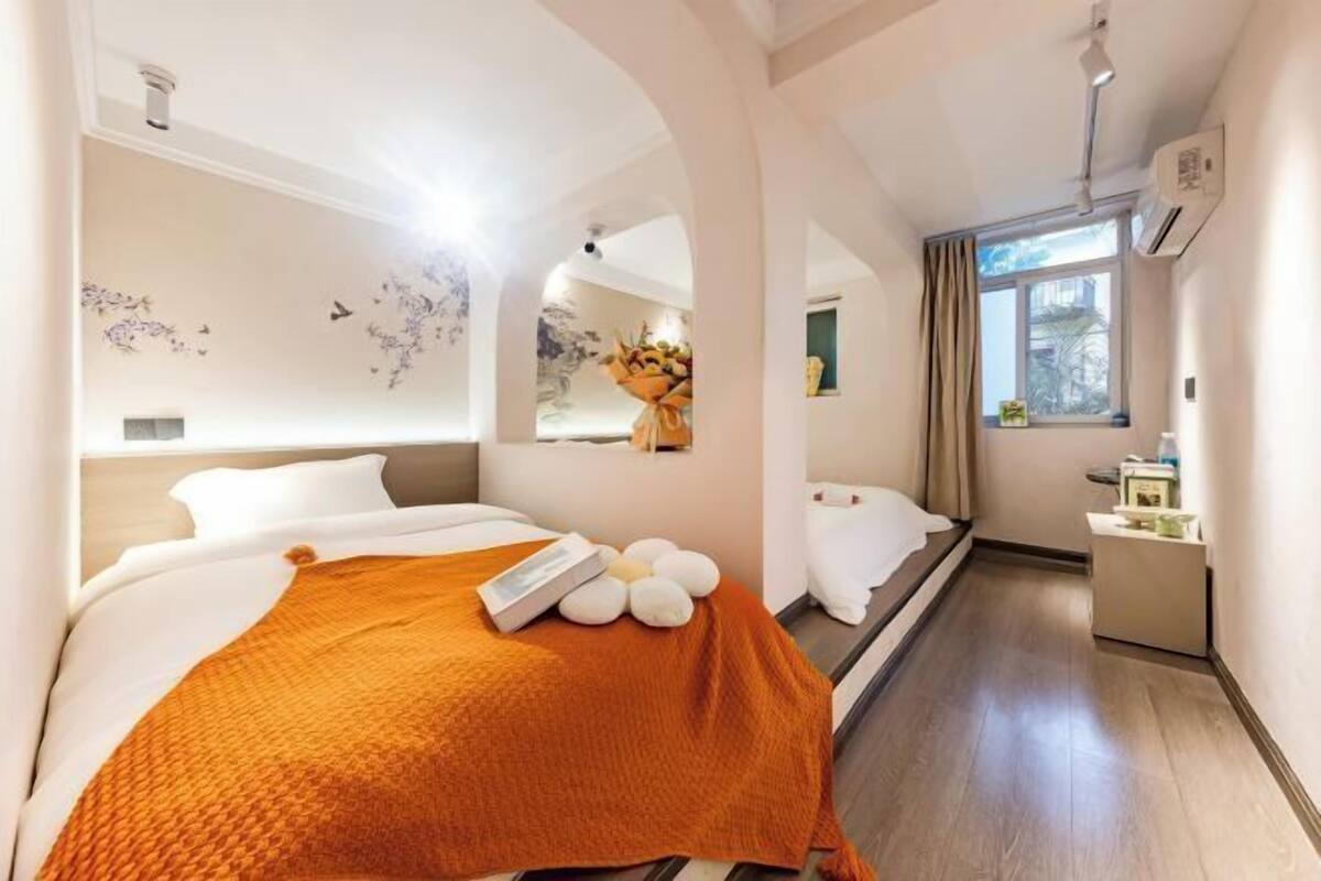 A hotel room with a bed, a small desk, a window, and a mirror.