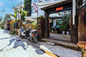 A street view with a shop entrance, a scooter parked outside, and potted plants.