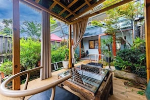 A covered outdoor seating area with a glass table, surrounded by potted plants and a wooden deck.